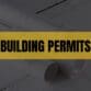 Text that says Building Permits on a light orange rectangle with construction plans in the background